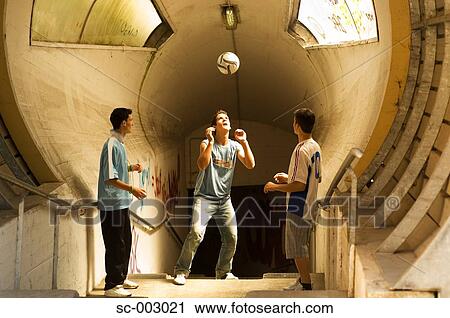 Stock Image - Teenage boys heading ball in tunnel. Fotosearch