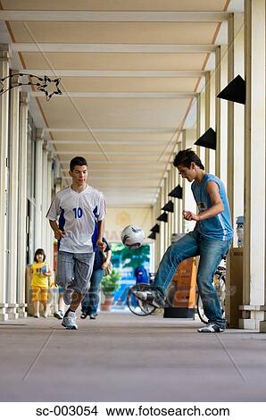 Picture - Teenage boys playing with soccer ball in town. Fotosearch
