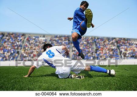 Soccer player kicking ball as defender slides in View Large Photo Image Picture - Soccer player kicking ball as defender slides in. Fotosearch