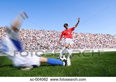 Soccer player kicking ball as defender slides in View Large Photo Image Stock Image - Soccer player kicking ball as defender slides in. Fotosearch