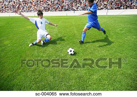 Soccer player kicking ball as defender slides in View Large Photo Image Stock Photography - Soccer player kicking ball as defender slides in. Fotosearch