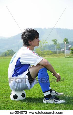 Stock Image - Soccer player sitting on ball. Fotosearch