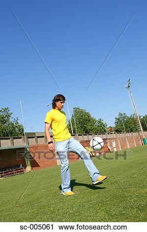 Stock Image - Young man in casual wear juggling soccer ball. Fotosearch