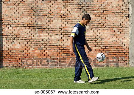 Stock Photo - Young man juggling soccer ball in front of brick wall. Fotosearch