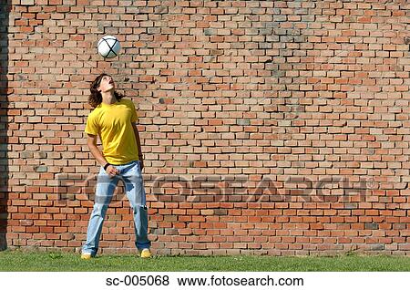 Stock Photo - Young man juggling soccer ball in front of brick wall. Fotosearch