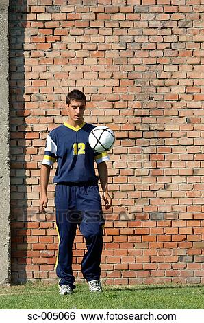 Stock Photograph - Young man juggling soccer ball in front of brick wall. Fotosearch