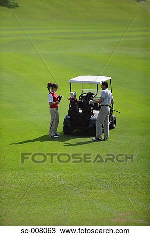 Stock Image - Couple holding golf clubs stand near a golf cart. Fotosearch