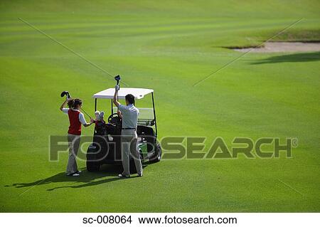 Picture - Couple putting their golf clubs into their golf bags on a golf cart. Fotosearch
