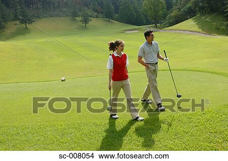 Picture - Couple walking down the fairway with their clubs. Fotosearch