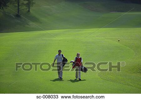 Couple walking on the fairway carrying their golf bags View Large Photo Image Stock Image - Couple walking on the fairway carrying their golf bags. Fotosearch