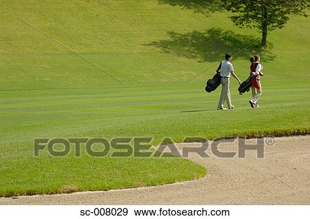 Couple with their golf bags walking near a bunker View Large Photo Image Stock Photo - Couple with their golf bags walking near a bunker. Fotosearch