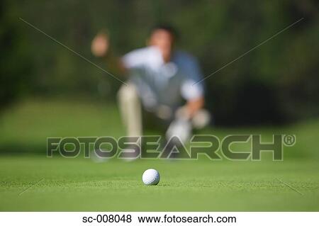Stock Photo - Golf ball in foreground as man lines up a putt. Fotosearch