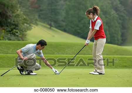 Stock Image - Male golfer sets a golf club held by a female partner on the tee ground. Fotosearch