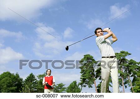 Stock Photo - Man hitting a golf shot with a woman looking on. Fotosearch