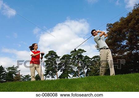 Stock Photo - Man hitting a golf shot with a woman looking on. Fotosearch