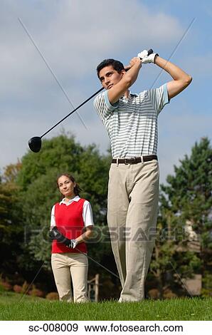 Stock Photo - Man hitting a golf shot with a woman looking on. Fotosearch
