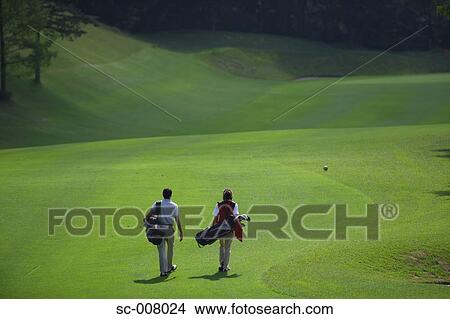 Picture - Rear view of a couple walking on the fairway as they carry their golf bags. Fotosearch