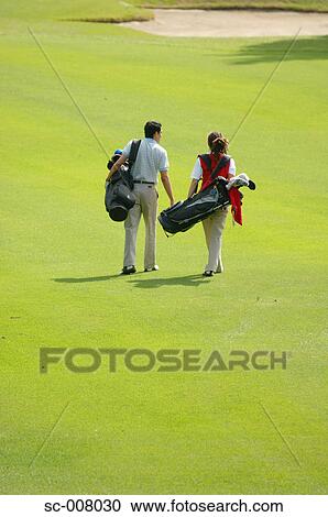Stock Image - Rear view of a couple walking on the fairway as they carry their golf bags. Fotosearch