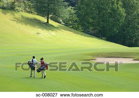 Stock Photo - Rear view of a couple walking on the fairway as they carry their golf bags. Fotosearch