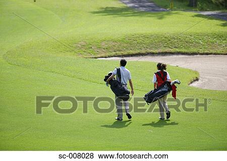 Stock Photo - Rear view of a couple walking on the fairway as they carry their golf bags. Fotosearch