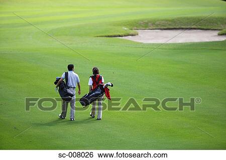 Stock Photograph - Rear view of a couple walking on the fairway as they carry their golf bags. Fotosearch