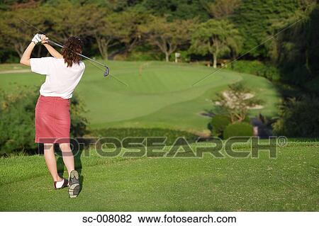 Stock Image - Rear view of a woman teeing off on a short hole. Fotosearch