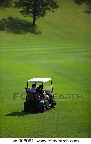 Stock Image - Rear view of two golfers sitting in a golf cart. Fotosearch