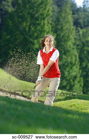 Stock Photo - A female golfer looks up after making a bunker shot. Fotosearch