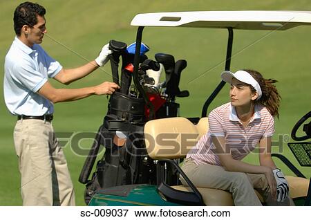 Stock Photo - A male golfer selects a club while his partner is seated in their golf cart. Fotosearch