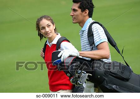 Couple carrying golf bags walking down the fairway View Large Photo Image Stock Image - Couple carrying golf bags walking down the fairway. Fotosearch