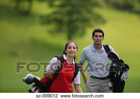 Stock Image - Couple carrying golf bags walking down the fairway. Fotosearch