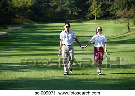 Stock Image - Couple holding hands as they walk down the fairway. Fotosearch