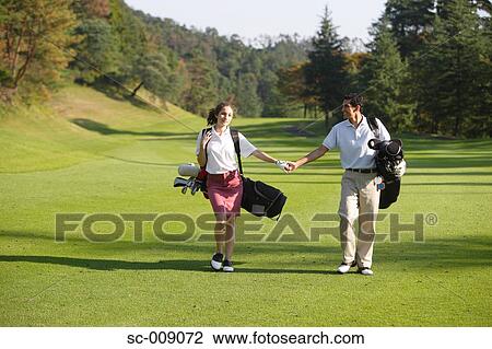 Stock Image - Couple holding hands as they walk down the fairway. Fotosearch