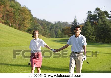 Stock Image - Couple holding hands as they walk down the fairway. Fotosearch