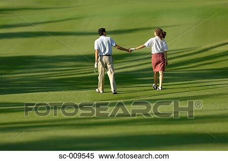 Stock Photography - Couple holding hands as they walk down the fairway. Fotosearch