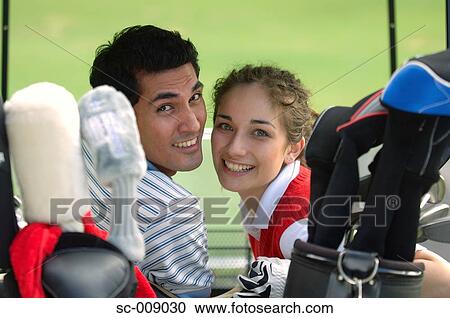 Stock Image - Couple looking back at the camera from their golf cart. Fotosearch