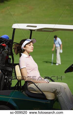 Female golfer catching some sunshine whilst her partner plays a shot View Large Photo Image Stock Image - Female golfer catching some sunshine whilst her partner plays a shot. Fotosearch