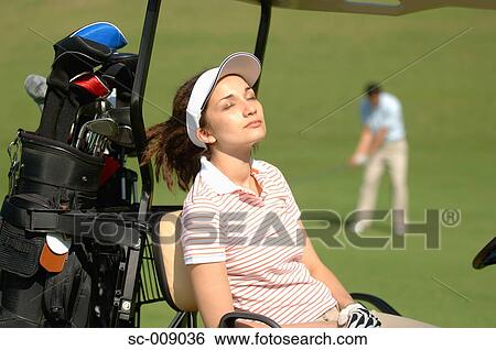 Female golfer catching some sunshine whilst her partner plays a shot View Large Photo Image Stock Photograph - Female golfer catching some sunshine whilst her partner plays a shot. Fotosearch