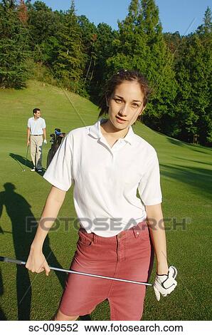Stock Image - Female golfer posing with her partner in the background. Fotosearch