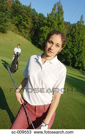 Stock Image - Female golfer posing with her partner in the background. Fotosearch