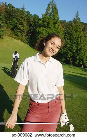 Stock Image - Female golfer smiling at the camera with a man in the background. Fotosearch