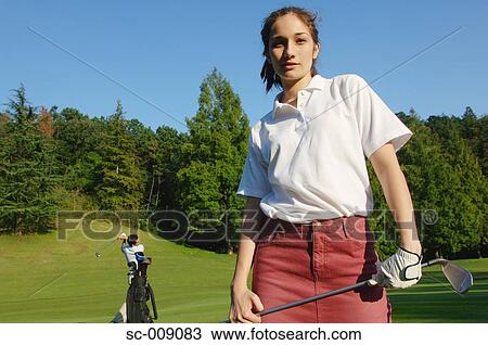 Stock Image - Female golfer smiling at the camera with a man in the background. Fotosearch