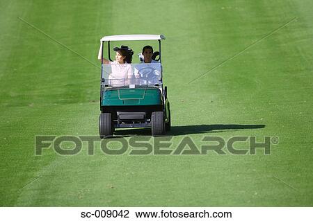 Stock Image - Front view of a couple riding in a golf cart. Fotosearch