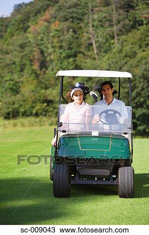 Stock Image - Front view of a couple seated in a golf cart. Fotosearch