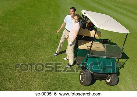 Stock Photograph - High angle view of couple standing near a golf cart. Fotosearch
