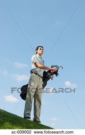 Stock Image - Low angle view of a man carrying a golf bag. Fotosearch