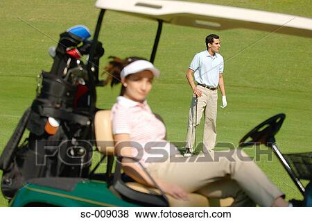 Stock Photo - Male golfer contemplating the course whilst his partner is seated in a golf cart. Fotosearch