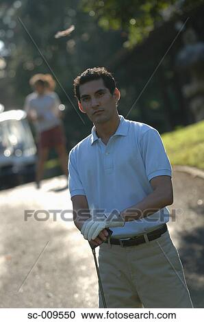Stock Image - Man posing in front of the camera holding a golf club. Fotosearch