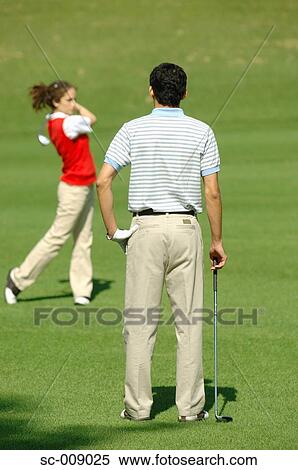 Stock Photography - Man watching a woman play a golf shot. Fotosearch