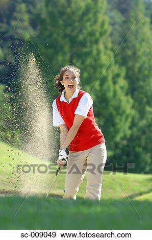 Stock Photo - Sand explosion as a female golfer plays a bunker shot. Fotosearch